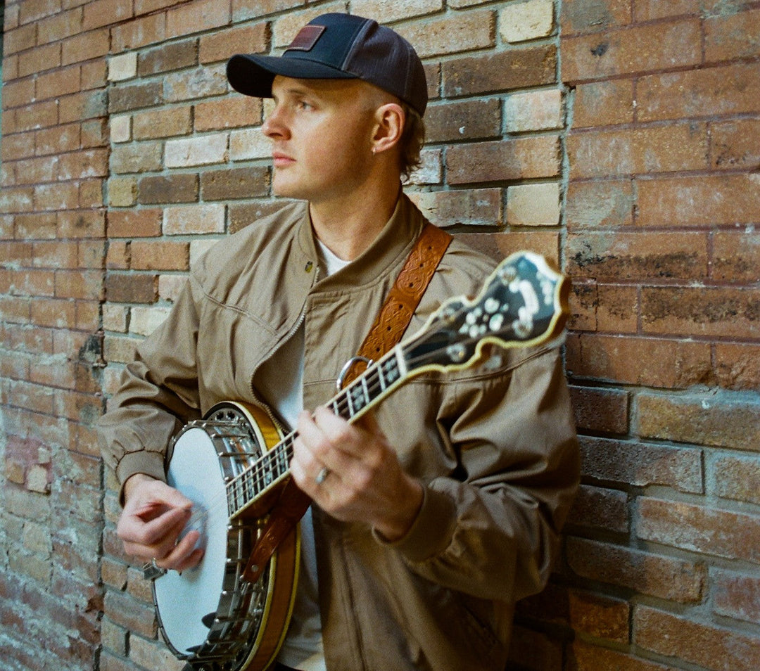 gavin strappe with his deering calico tenor banjo leaning against a red brick wall