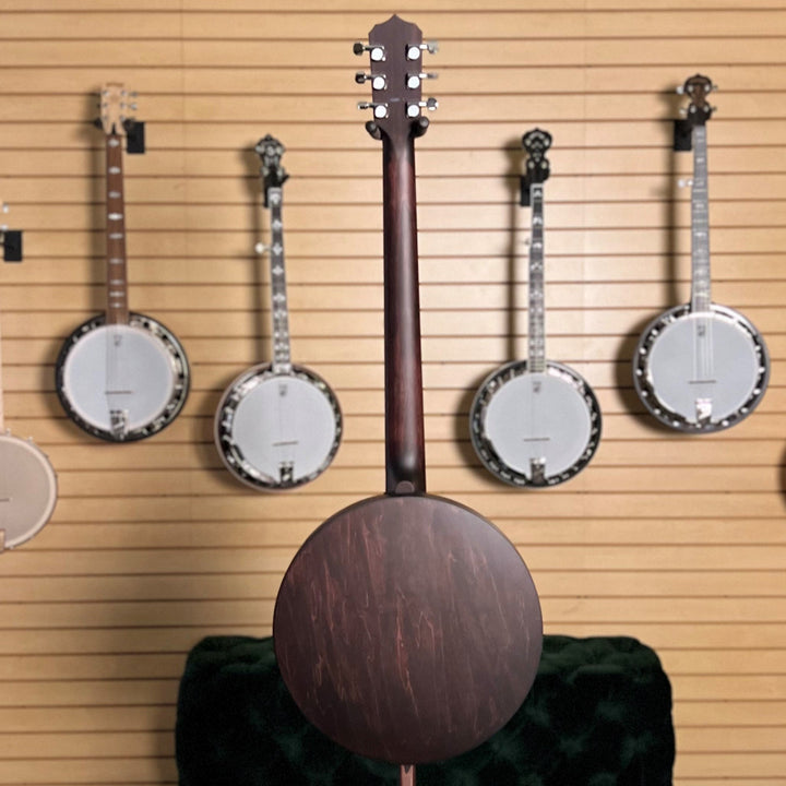 dark stained six string banjo full back in front of a collection of banjos displayed against a wall with framed pictures.