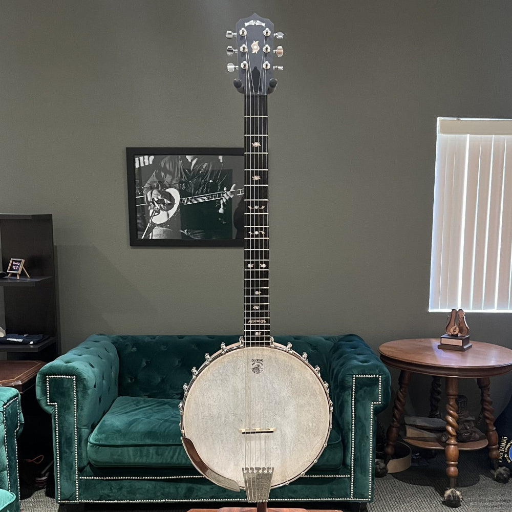 Banjo on a stand in a room with green couches and framed pictures on the wall.