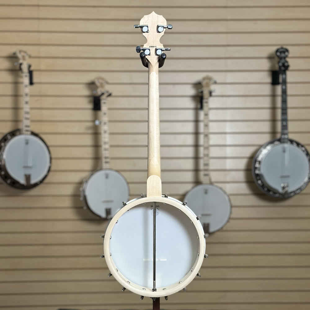 short scale 19 fret tenor banjo, natural blonde finish in front of wooden wall with banjo instruments hanging in the background. 