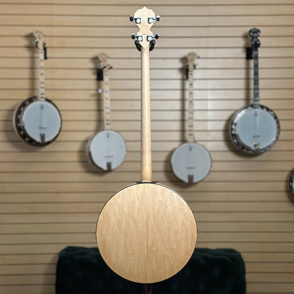 22 fret 4 string  banjo, natural blonde finish in front of wooden wall with banjo instruments hanging in the background. 