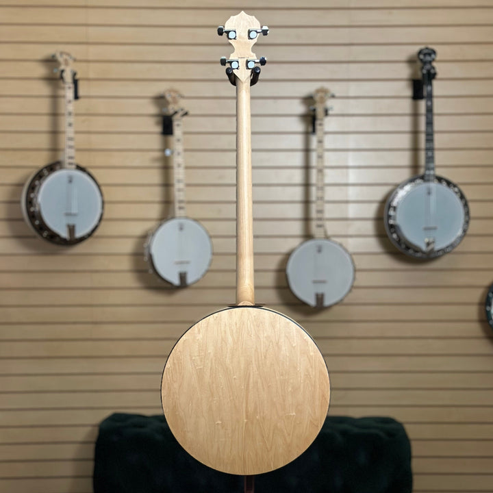 22 fret 4 string  banjo, natural blonde finish in front of wooden wall with banjo instruments hanging in the background. 