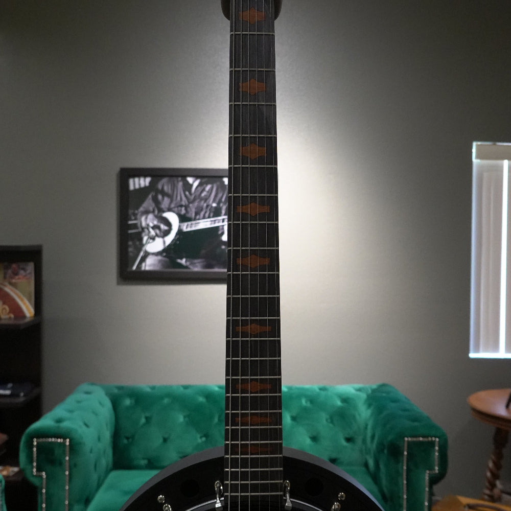 Black banjo in a room with green couch and television displaying a guitar.