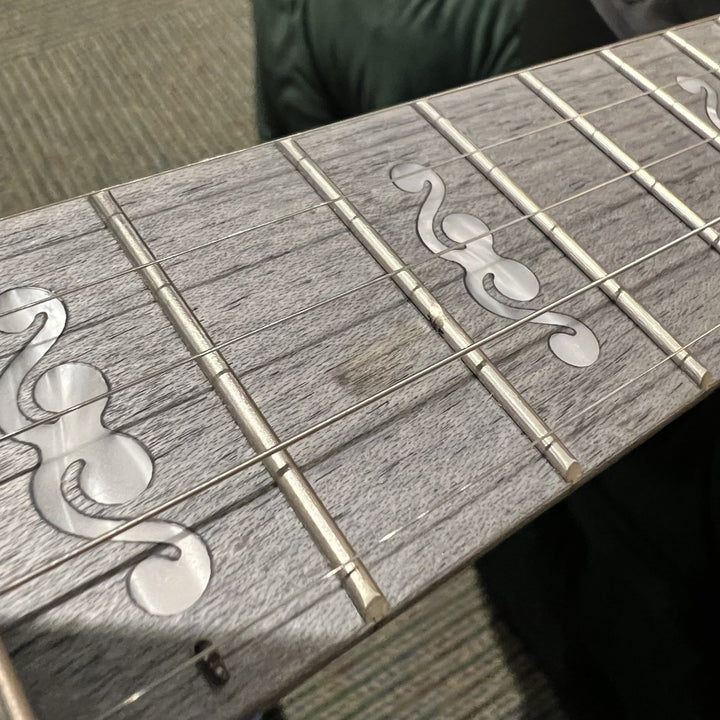 Close-up of a guitar fretboard with a weathered gray wood finish and clear maple inlays, resting on a carpeted floor.