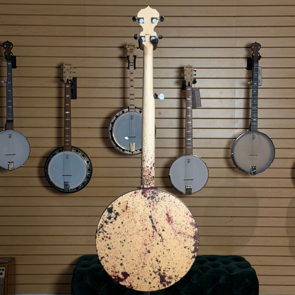 back of banjo with red, black, and brown splatter stain in front of wall of banjos.