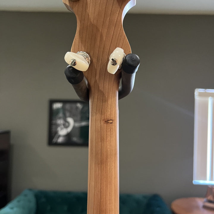 Close-up of a wooden guitar neck with tuning pegs against a blurred indoor background