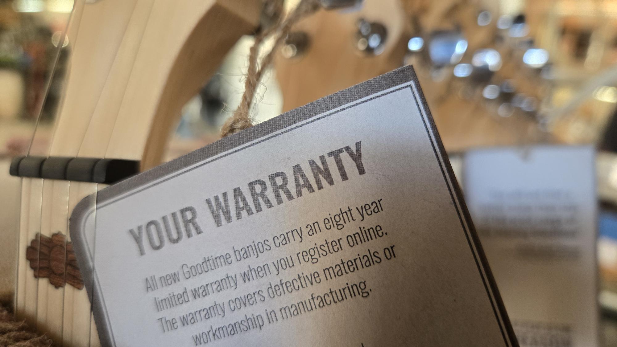 Close-up of a warranty card attached to a banjo, with a blurred background.